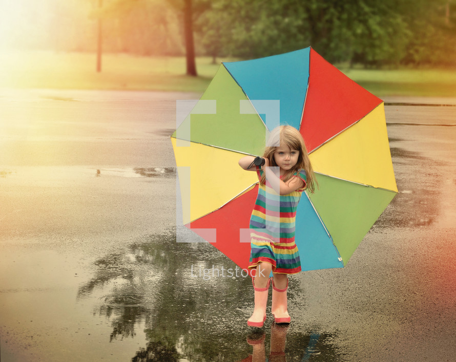 a little girl in rain boots carrying an umbrella 