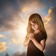 a little girl with glasses praying at sunrise 