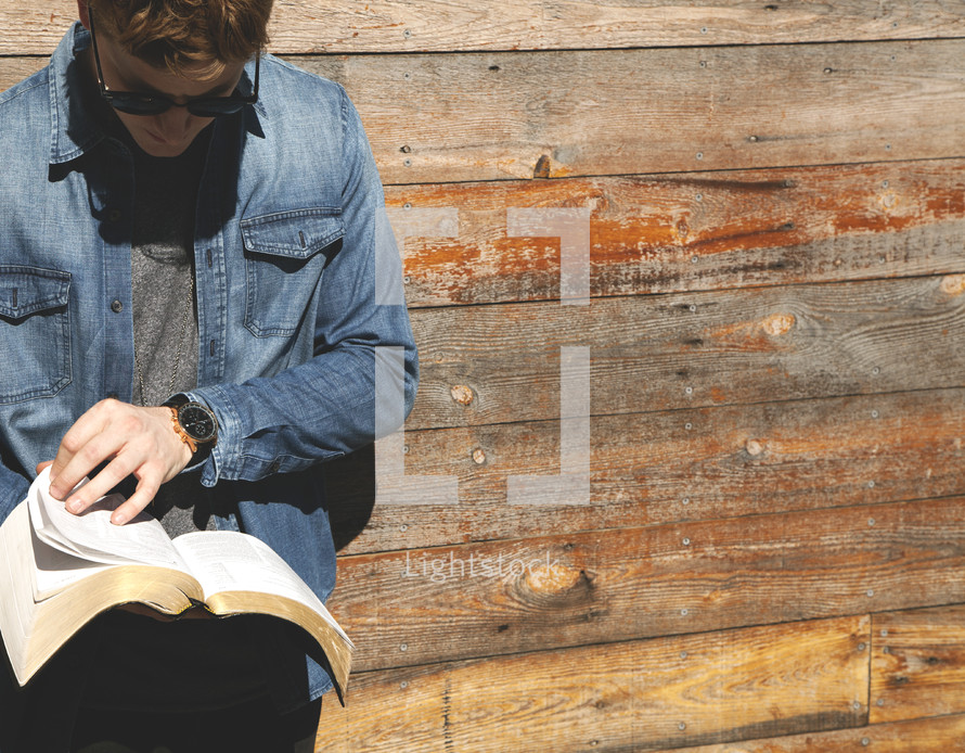 a man reading a Bible in front of a wall of wood 