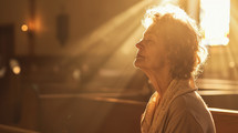 Sunlit prayer. Aged woman praying in the church in the sunbeams shining through the window.