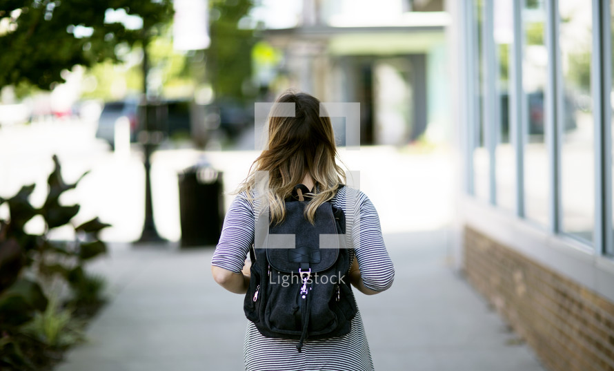 woman with a book bag walking down a sidewalk 