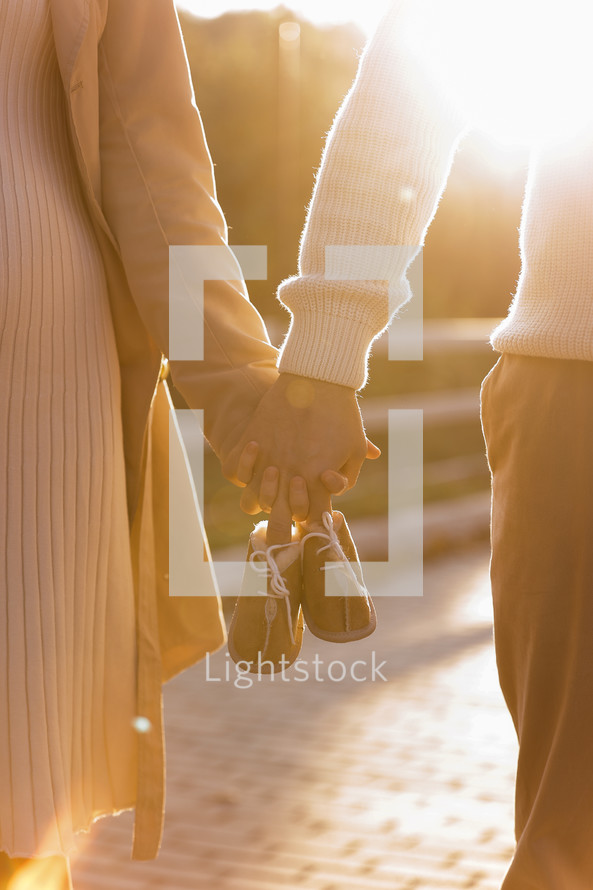 Cropped photo of couple, man and pregnant wife are holding hands and warm baby shoes on nature autumn background. Future parents waiting for the baby. The concept of Mother's Day and Women's Day