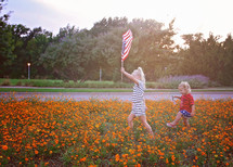 children marching through a field of orange flowers holding an American flag 
