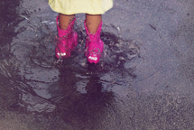A child wearing pink rain boots standing in a puddle.