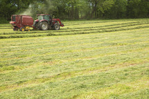 A red tractor harvesting a crop in a green field.