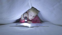boy reading a book under the covers 