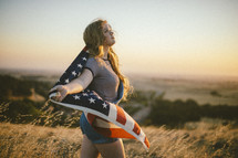a teen girl carrying an American flag in a field at sunset 
