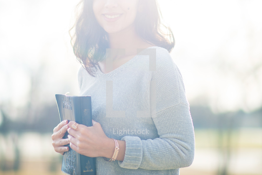 a young woman holding a Bible against her chest 