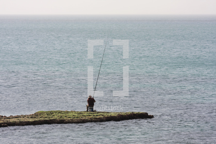 Fisherman sits on a finger of land and fishes in the sea.