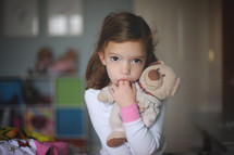 child sucking her fingers holding a teddy bear 