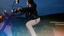 Hipster stylish motorcyclist woman sitting on vintage-styled motorcycle. Young female driver at night on roadway. Trip, freedom, classic motorbike concept. High quality photo