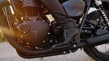 Legs of stylish motorcyclist woman sitting on classic bike. Black retro-styled motorcycle. Details of vintage design of brand-new motorbike. Sun flare, outdoor. High quality photo