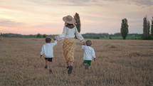 Two ukrainian boys and mother running together on open area wheat field after harvesting. Family friends holding hands. Children is our future. Nature background. Happy childhood.