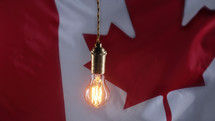 Flickering classic antique Edison Tungsten filament lamp on waving canadian flag background. 