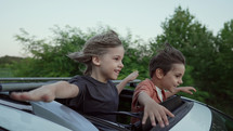 Adorable happy little kids stands in open car sunroof during road trip in countryside, rural landscape at summer. Concept of family leisure, active traveling. High quality