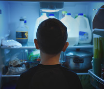 a boy child looking into a refrigerator 