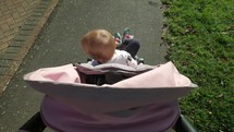 Slow motion steady cam view of a Caucasian toddler in a stroller 