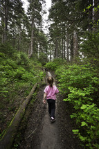 girl child walking uphill on a path through a forest 