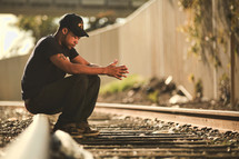 Man sitting on railroad tracks with head bowed