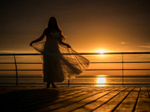 Silhouette of a woman in a wedding dress standing by the ocean in the sunlight.