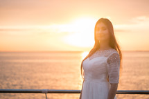 Woman in a wedding dress standing by the ocean in the sunlight