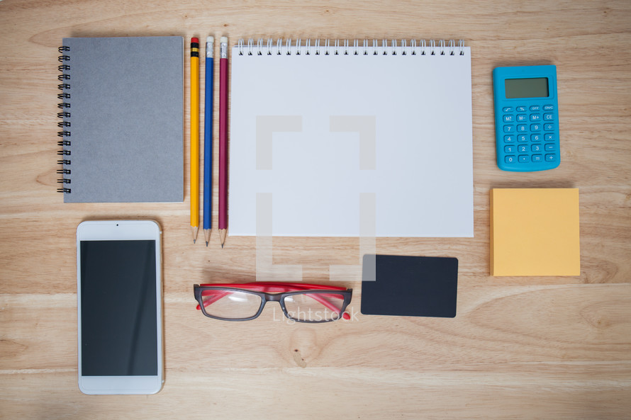 iPhone, notepad, reading glasses, pencils, sketchbook, calculator, sticky notes, on a desk 