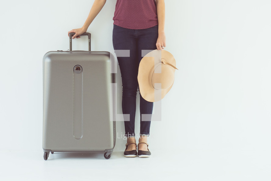 a woman standing with a sunhat and suitcase 