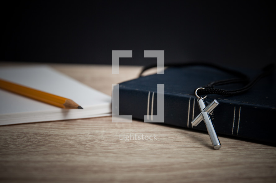 pencil, notepad, Bible, and cross necklace on a desk 