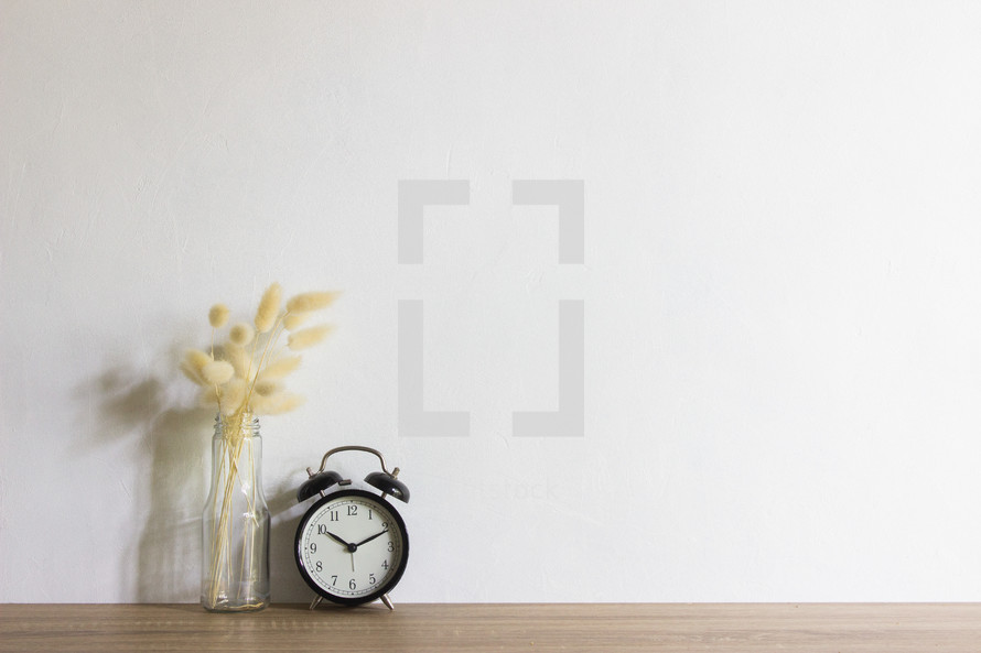 vase and alarm clock against a plain white wall 