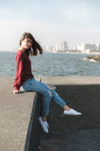 a young woman sitting on the edge of a concrete wall 