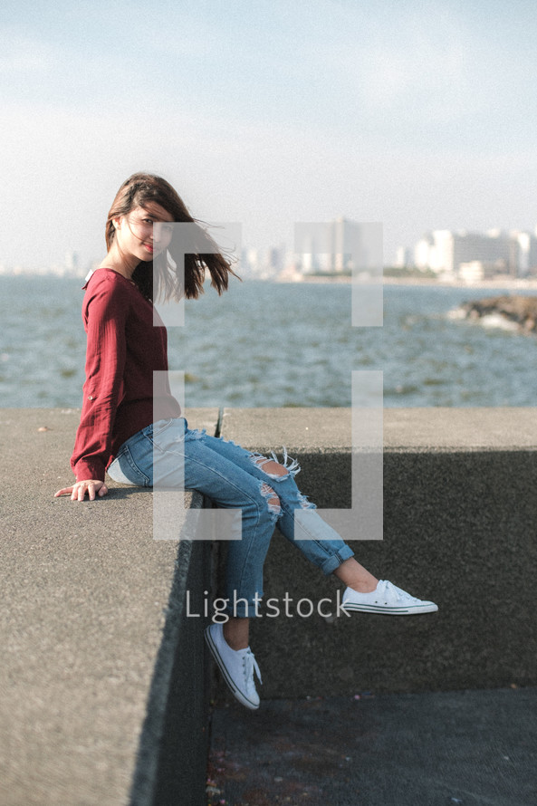a young woman sitting on the edge of a concrete wall 