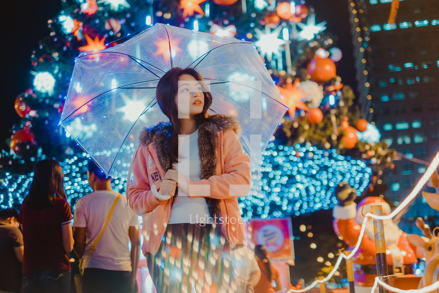 a woman holding an umbrella in front of a Christmas tree