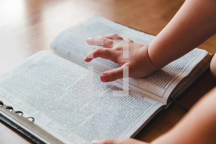 Little boy's hand touching an open Bible.
