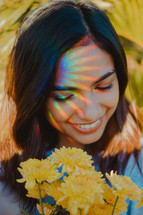 rainbow burst on a woman's face as she holding a bouquet of yellow flowers 