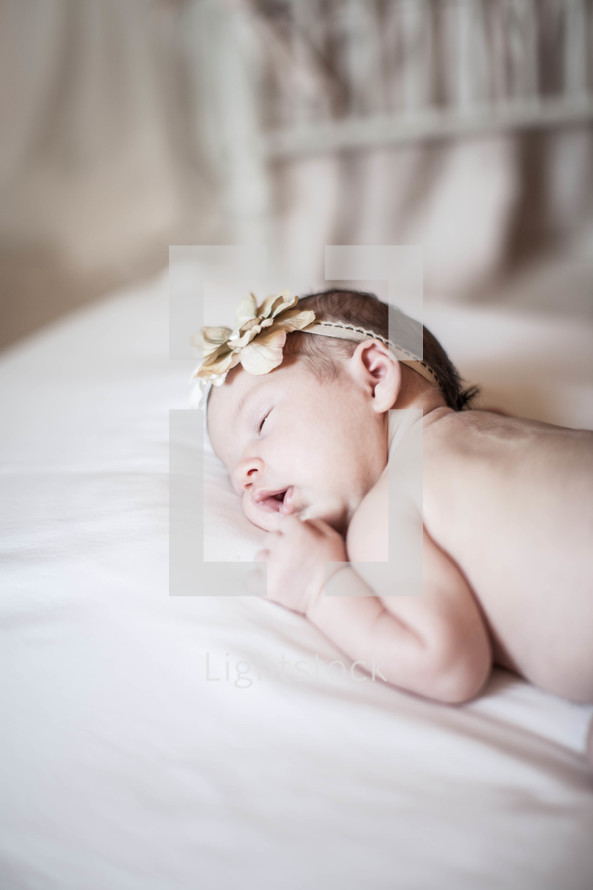 Baby with headband sleeping on tummy in crib.