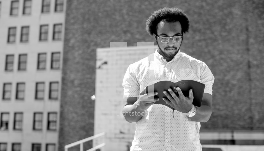 an African American man standing reading a Bible in a city 