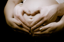 expecting couple making a heart with their hands on a pregnant belly 
