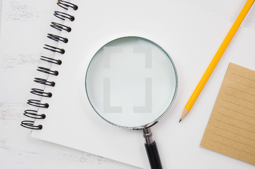 magnifying glass on a spiral notebook and pencil 