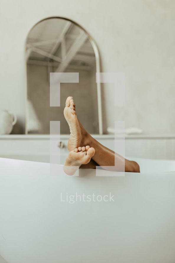 Woman's bare feet hanging over bathtub in bathroom