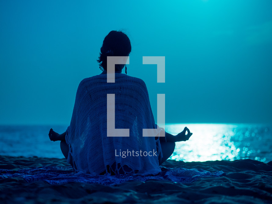 Young girl sitting at night on beach against moon road on sea and meditating frame shape silhouette
