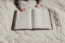 infants hands on the pages of a Bible 