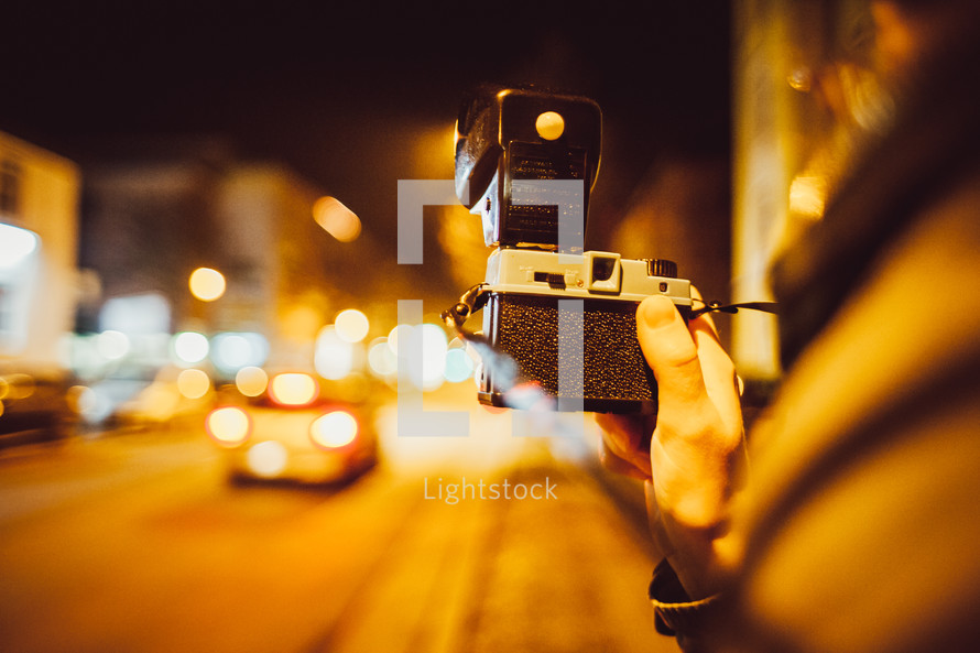 person standing on a city sidewalk at night taking pictures 