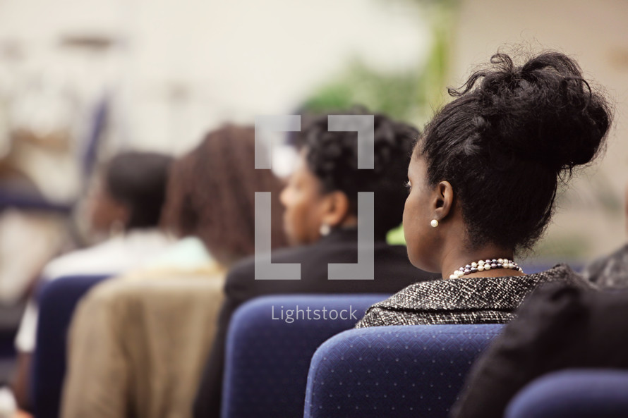 Profile of woman  seated in church service; attentively listening and watching preaching, women in background