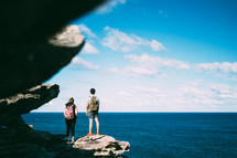 man and woman standing on the edge of a cliff over the ocean 