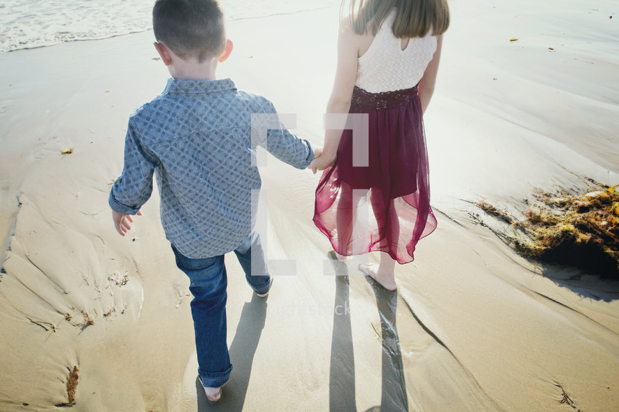 sibling walking holding hands on a beach 