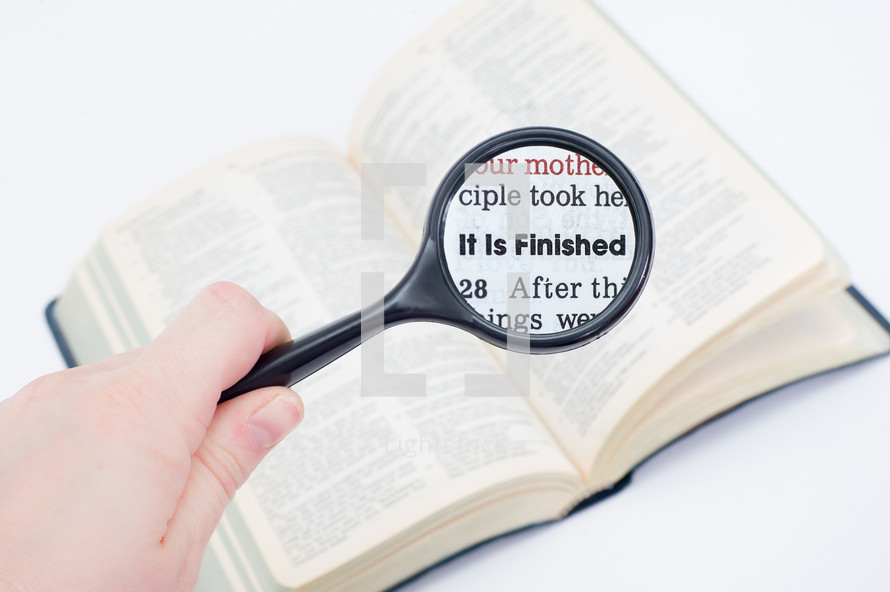 magnifying glass over the pages of a Bible - It is finished 