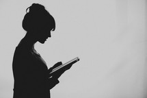 A young woman silhouetted reading her Bible