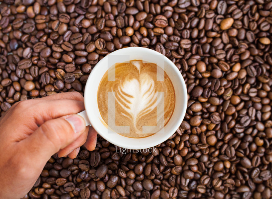 Hand holding Coffee cup on a background of Coffee beans.