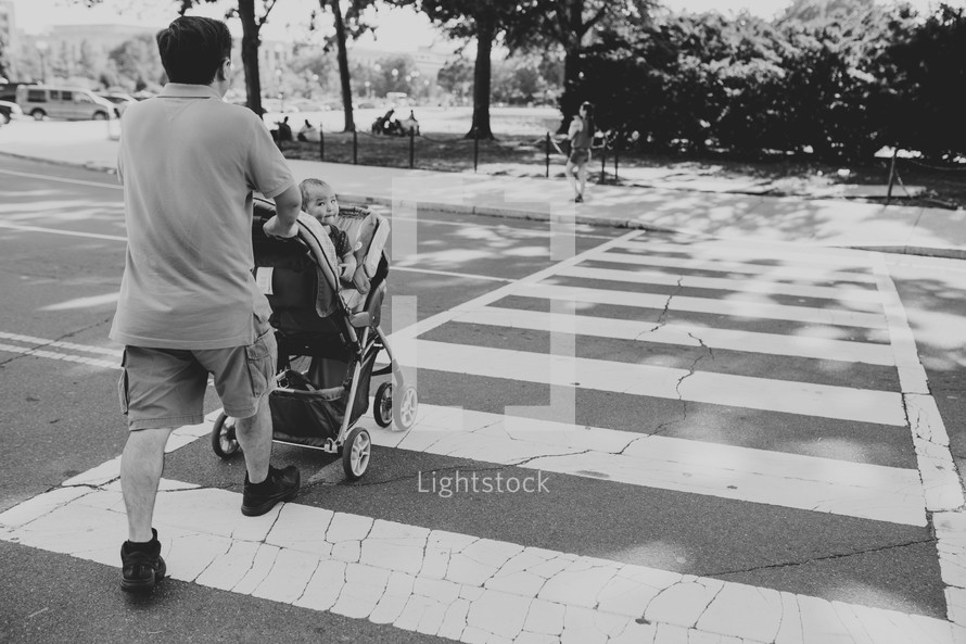 a father pushing his baby in a stroller across a crosswalk 