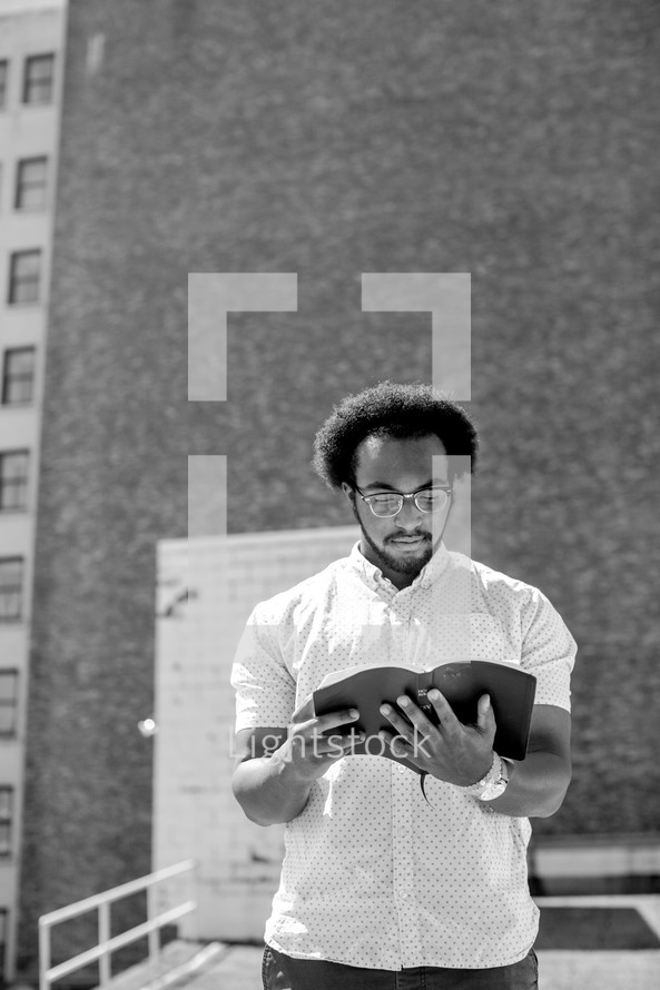 An African American man standing reading a Bible in a city 